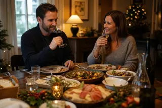 Two people at a festive dinner table tasting wine and food pairings in a softly lit, welcoming home setting.